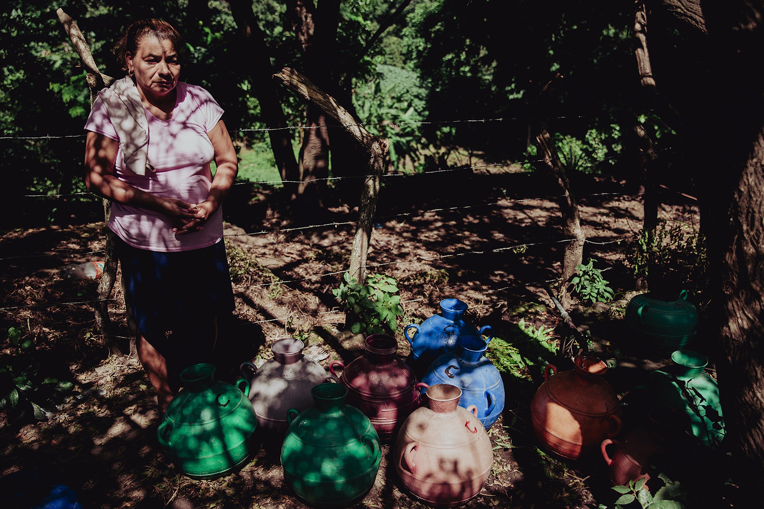 Consuelo del Carmen Cruz espera a un lado de una calle polvorienta a que sus cántaros se llenen de agua en un chorro comunal en el cantón Loma Alta, del municipio de Berlín, departamento de Usulután, El Salvador. Foto de El Faro: Carlos Barrera