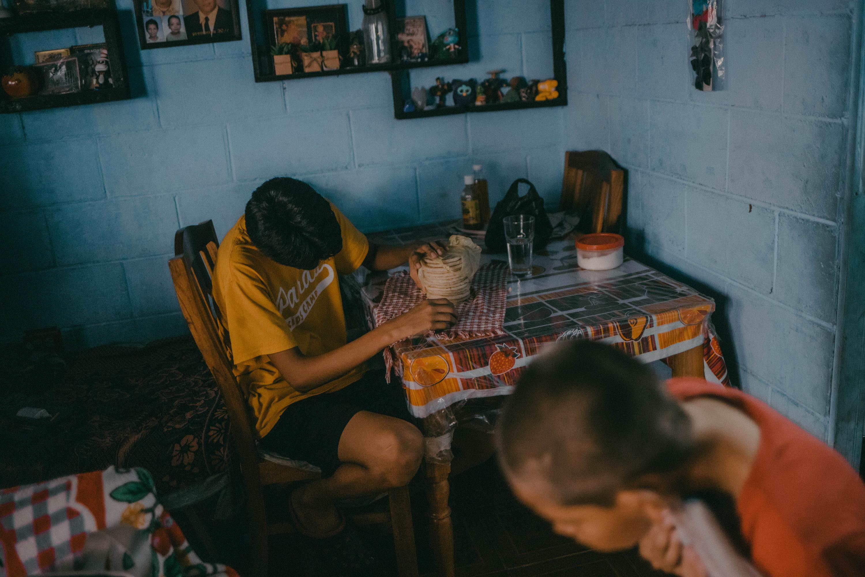 La Nueva Esperanza es de las pocas comunidades que quedan en el corazón de la capitalina colonia Escalón. Allí, a unas cuadras del World Trade Center, decenas de familias viven apuñadas en pequeñas casas. Una de esas es la familia Ábrego que, liderada por Cecilia, trata de sobrevivir. Hace unos meses, durante el régimen de excepción, uno de los hijos de Cecilia fue capturado, a pesar de que su familia había sido víctima de las pandillas: dos hijos más tuvieron que huir hacia Estados Unidos por la violencia pandillera de la zona. Celia se pasa los días recolectando recipientes de plástico para vender y con eso comprar un paquete de alimentos y enseres básicos y llevarlo al centro penitenciario donde está su hijo. En casa, se saltan tiempos de comida por la escasez o comen únicamente arroz con tortillas. La carne no es opción. Al mediodía cuando las tortillas llegan, Ricardo Alexánder Ábrego, de 16 años, las cuenta para racionarlas y que alcancen para al menos dos días.