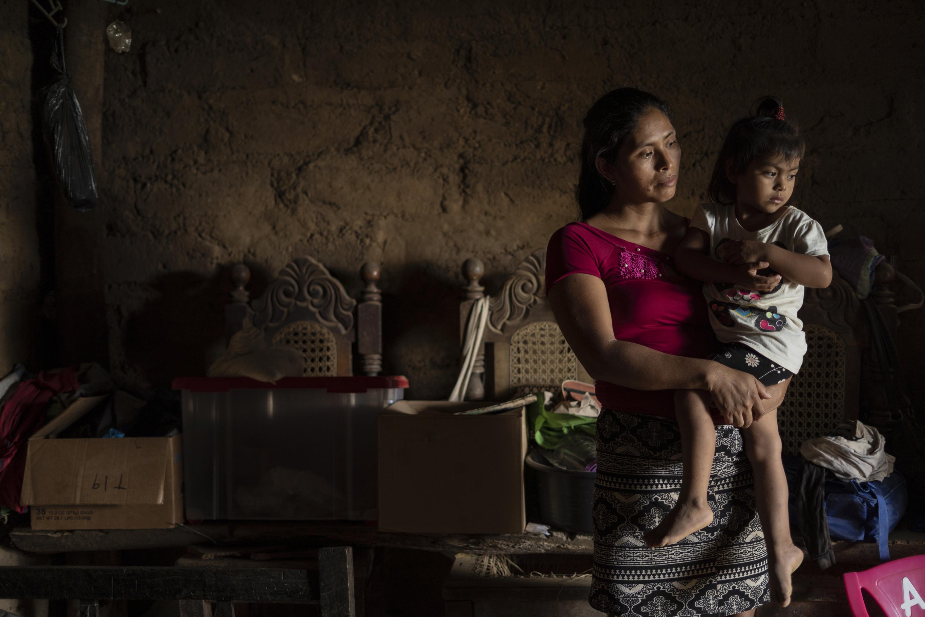 Maura Dolores carga a Deysi Nohemy López, de tres años, en su vivienda del caserío El Jícaro Centro, del municipio de Tacuba, departamento de Ahuachapán. La despensa de Maura son un par de cajas de cartón y un recipiente plástico donde quedan algunos sobres de café instantáneo, un poco de arroz, jabones, consomés y toallas sanitarias. Desde la captura de su esposo bajo el régimen de excepción, Maura y sus cuatro hijos deben sacrificar un tiempo de comida. Cuando comen, hacen malabares, como repartir en una semana cuatro huevos entre cinco personas. 