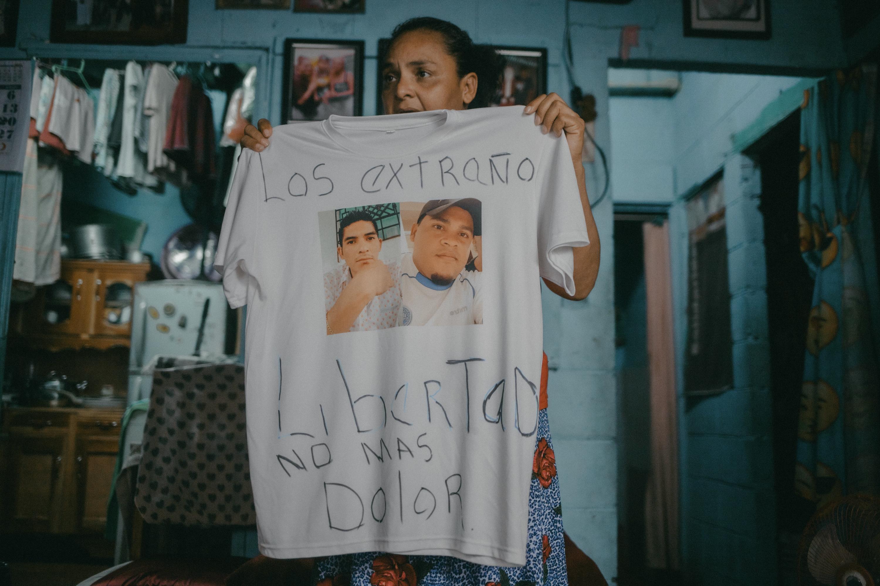 Cecilia Ábrego holds up a T-shirt with pictures of her son and her brother, who were arrested during the state of exception, and whom she now prioritizes by sending care packages with food from her scarce home supply. Photo Carlos Barrera