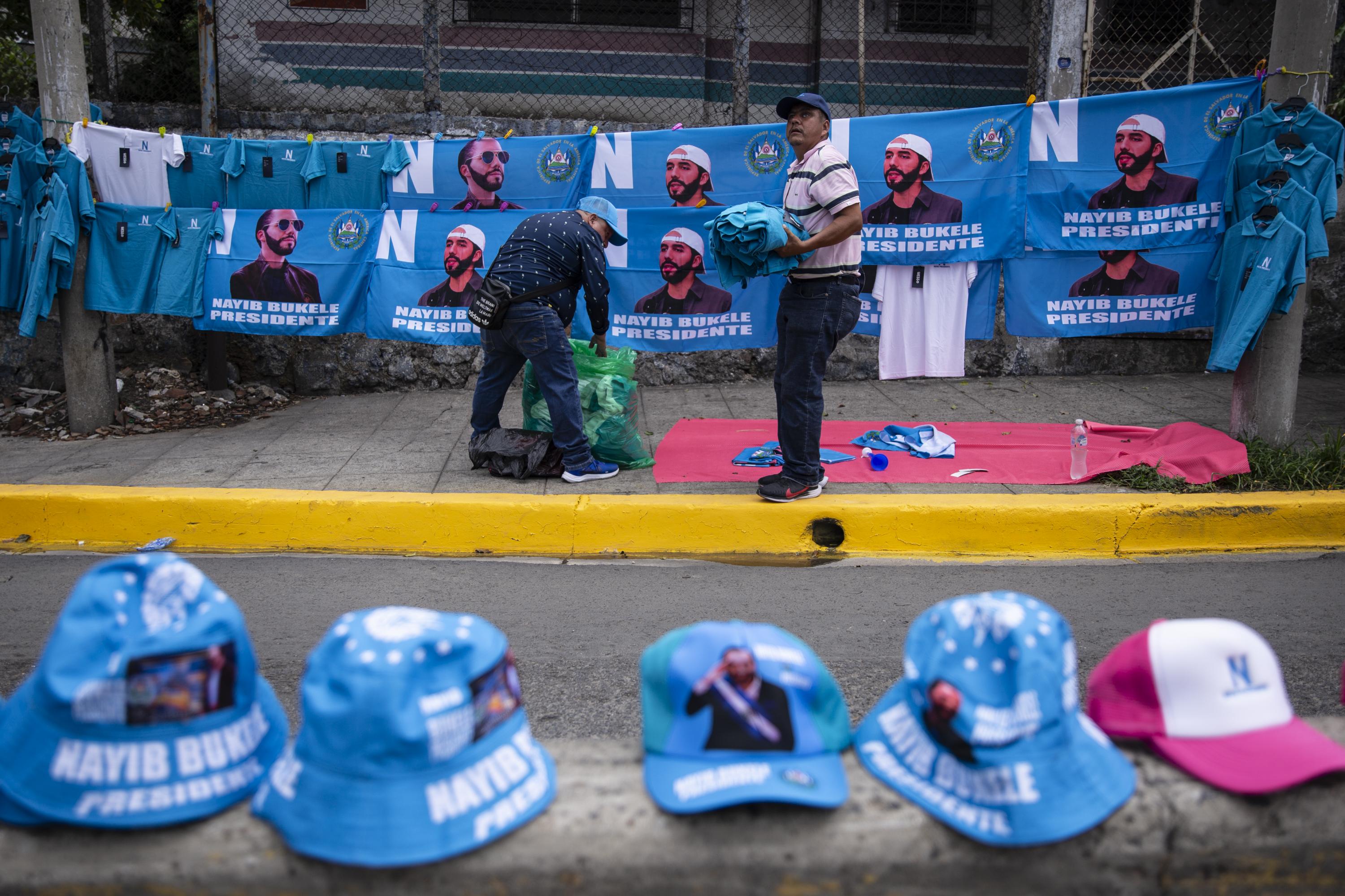 Fernando Cornejo Chávez (derecha) fue empleado del departamento de capacitación de la Asamblea Legislativa. Fue despedido unos meses después de que Ernesto Castro asumiera como presidente en 2021. Cornejo no encontró trabajo desde entonces y tuvo que salir a las calles a vender. El 1 de junio se estableció en los alrededores de la plaza Barrios para vender prendas con la imagen de Nayib Bukele. Foto de El Faro: Víctor Peña. 